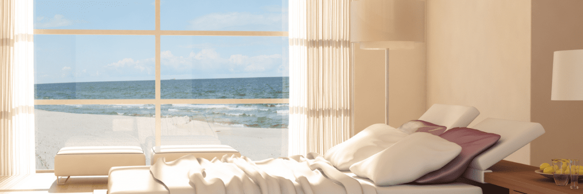 Wide shot of sleek, minimalistic bedroom in beach house with large windows.