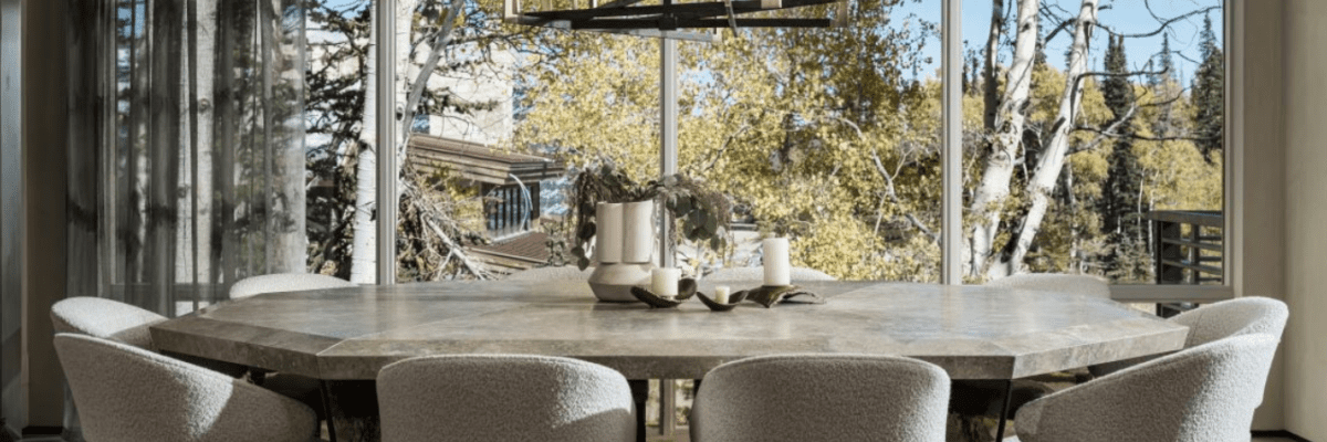 Wide shot of modern dining room with large window with track system from Vesta’s Eco-Deco Collection. Large stone dining table is in the center of the shot with ten sherpa dining chairs surrounding it.