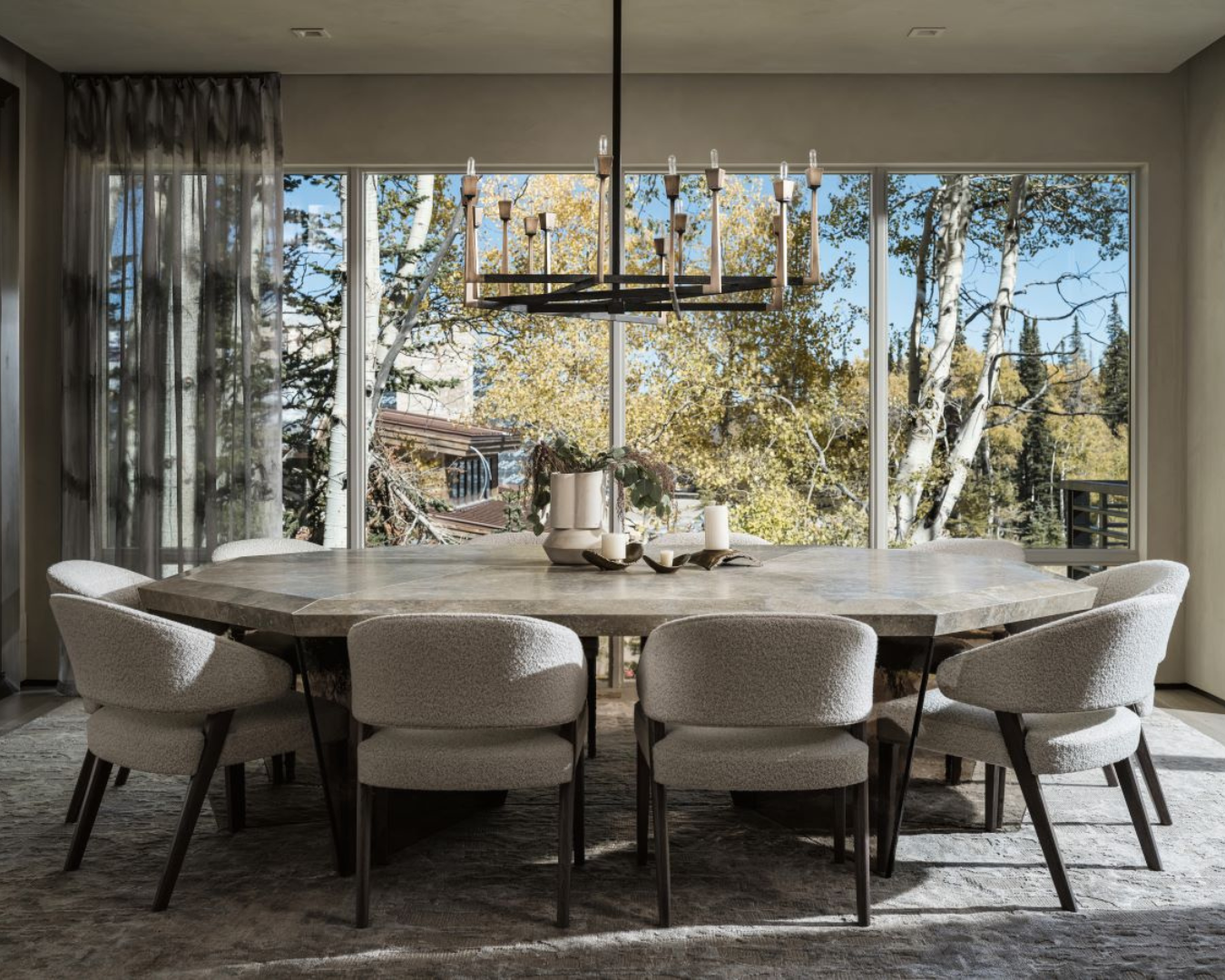 Wide shot of modern dining room with large window with track system from Vesta’s Eco-Deco Collection. Large stone dining table is in the center of the shot with ten sherpa dining chairs surrounding it.