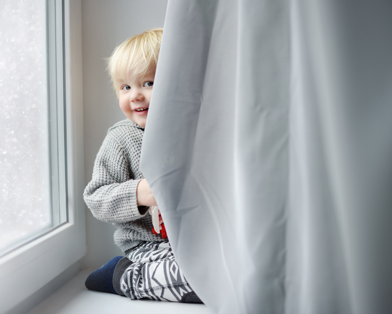 Blonde, male, toddler peeking behind drapery, smiling at camera.