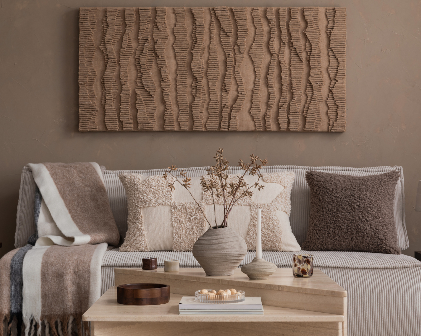 Cozy living room with ogg white couch with muted neutral and brown pillows, simple light wooden table, and neutral and light brown decor.